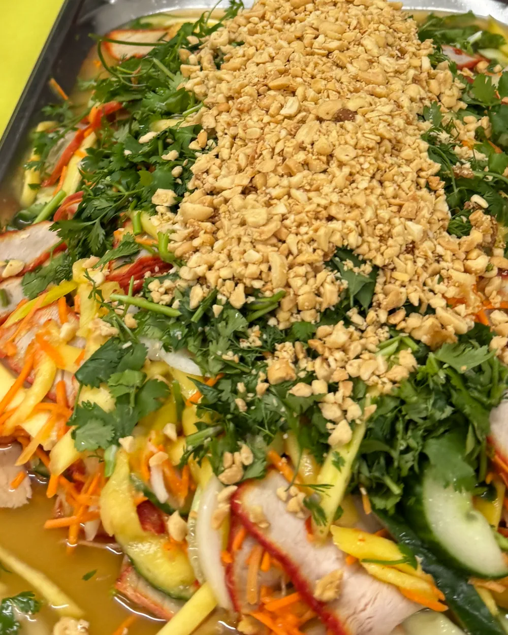 Un grand plat de salade mango à partager : mangue, porc laqué, concombre, carotte, herbes fraîches et cacahuètes concassées.
