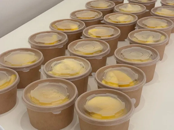 Une vingtaine de pots individuels en carton, fermés par un couvercle transparent, alignés sur une table.