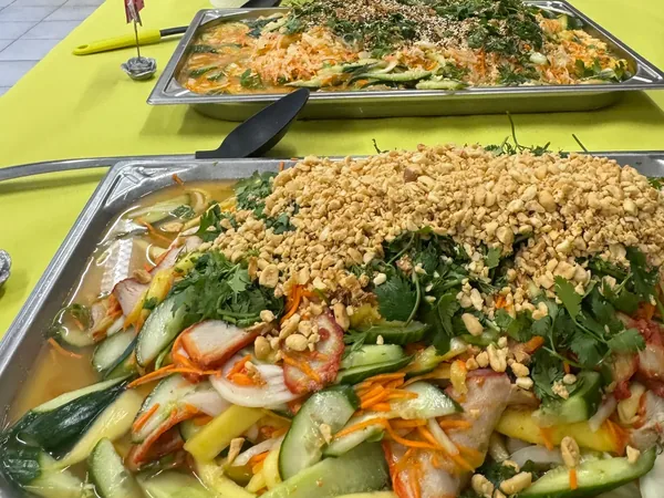 Deux plats de salade à partager sur une nappe jaune, l'un couvert de cacahuètes concassées.
